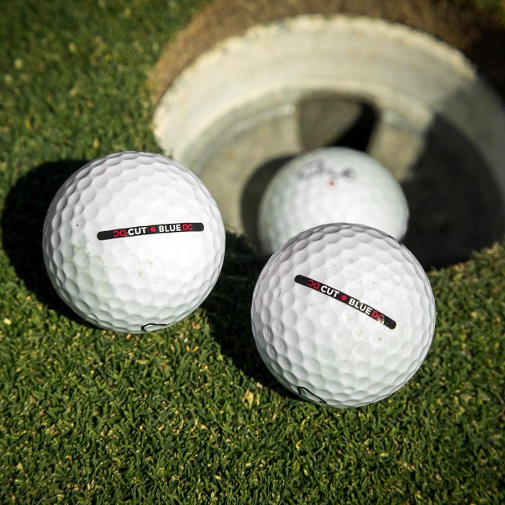 Two Cut Blue Golf Balls Next to Hole and One Cut Blue Ball In the Cup