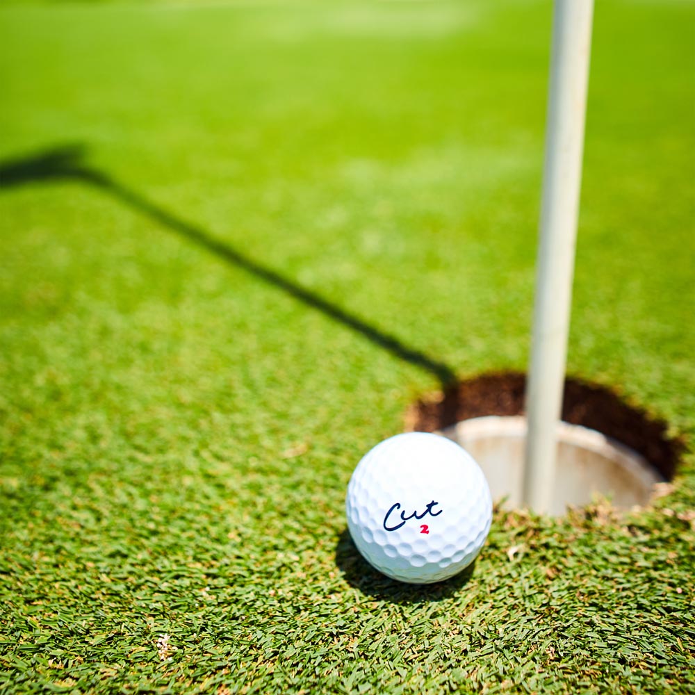 Cut Red Golf Ball Next to Golf Hole With Pin In It