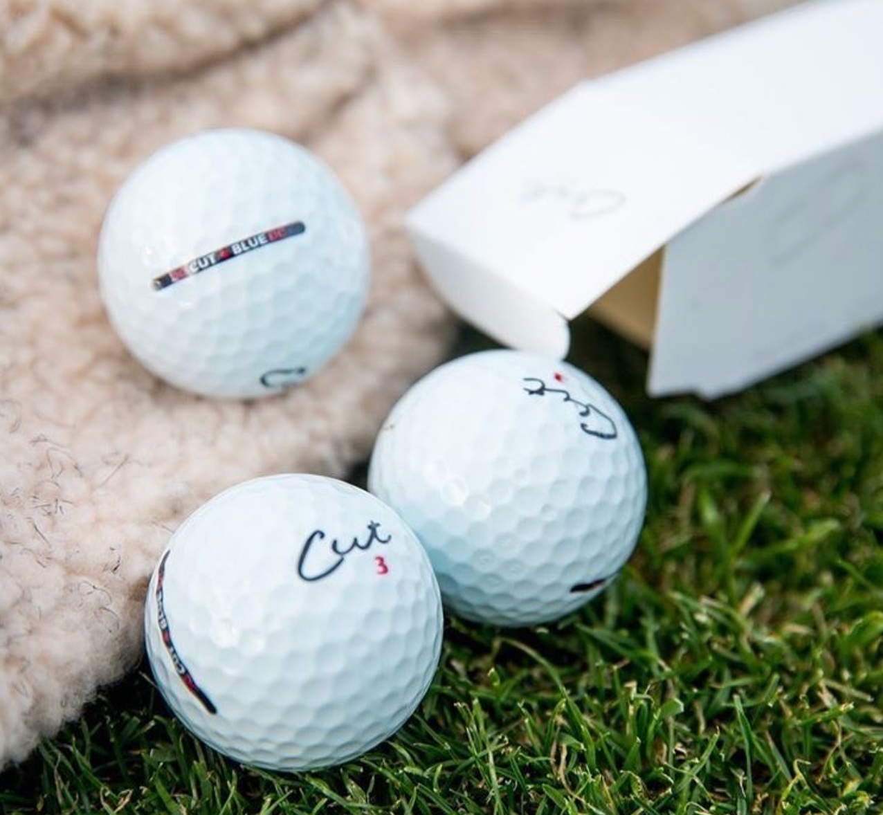 Three Cut Blue Golf Balls Out of a Sleeve With Box Next To It
