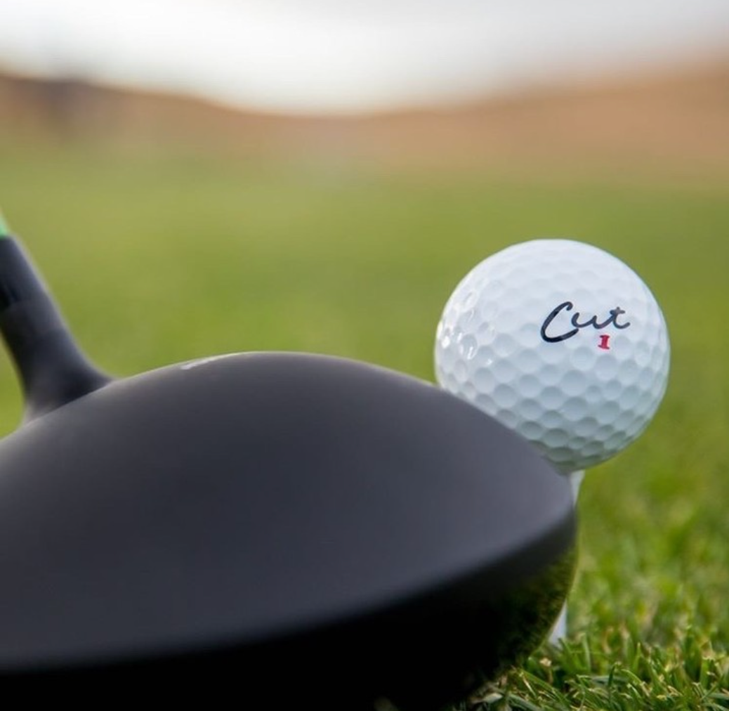 Cut Red Golf Ball On a White Tee With a Driver Next To It